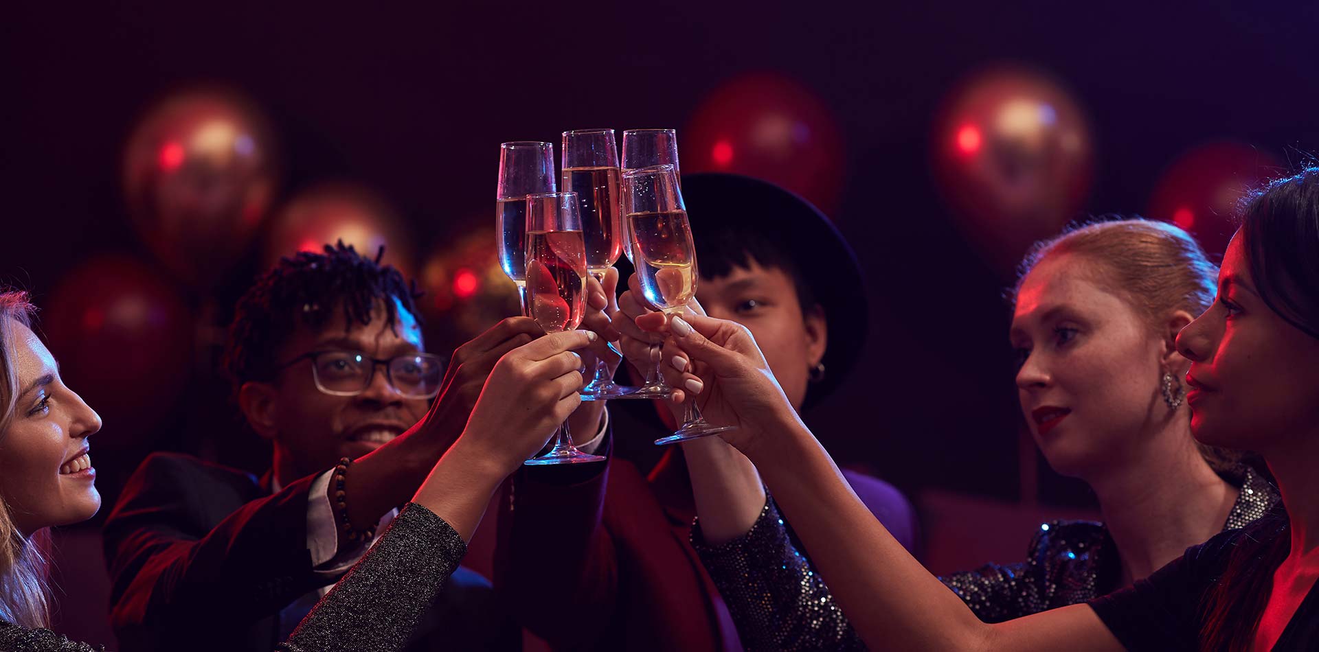 Group of elegant young people raising champagne glasses while enjoying party in nightclub.