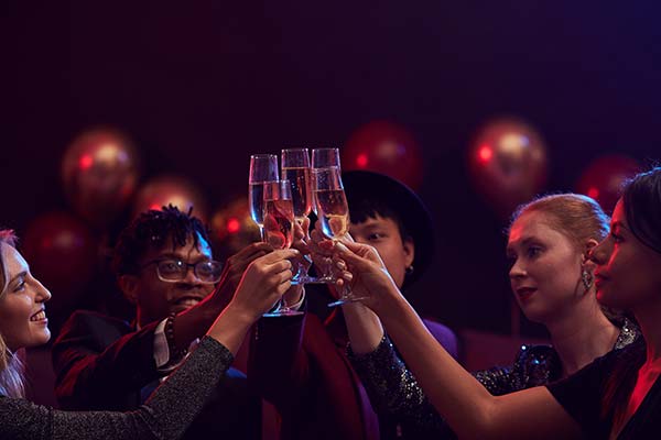 Group of elegant young people raising champagne glasses while enjoying party in nightclub.